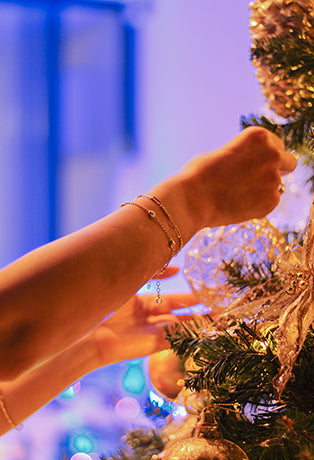 Mano con pulseras de oro decorando un árbol de navidad