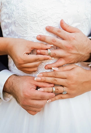 Las manos de una pareja recién casada sobre el frente del vestido de la novia, poniéndose sus argollas mutuamente. 