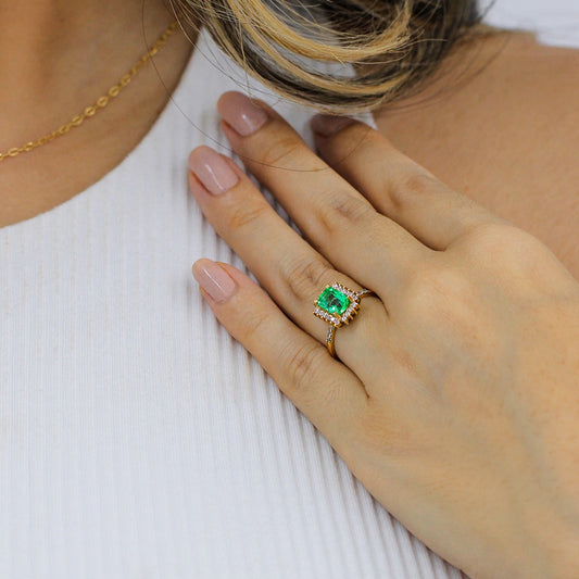 Mano de mujer con anillo en oro amarillo de 18 quilates y esmeralda en color verde con cristales de color blanco, hecho en Joyería Caracas. 